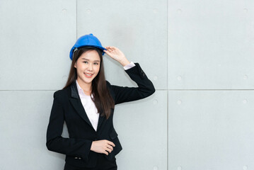 Portrait images of an Asian business woman, attractive and young, wearing and holding worker helmet, with wall background, to business and engineer concept.