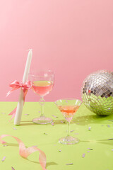 Celebration party for new year or holiday concept with two glasses filled with pink wine displayed with a candle and a disco ball. Pink background for girly style