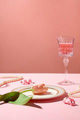 Wall Mural - A flower is lying on a plate, surrounded by pearl necklaces and pink paper fireworks. A glass filled with pink wine featured. Holiday party concept