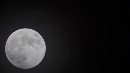 Wall Mural - dark mystical clouds passing in front of white full moon against black background - static
