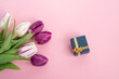Bright colorful purple and white flowers tulips lie on a pink background with a gift box