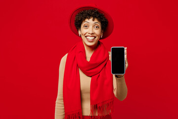 Poster - Young happy woman of African American ethnicity she wears beige sweater hat scarf hold use mobile cell phone with blank screen workspace area isolated on plain red background studio Lifestyle concept