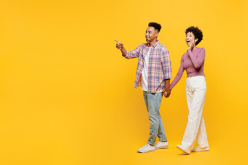 Wall Mural - Full body young couple two friend family man woman of African American ethnicity in purple casual clothes together walk go stroll point index finger aside on area isolated on plain yellow background