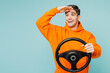 Young happy man he wears orange hoody casual clothes hold steering wheel driving car look far away distance isolated on plain pastel light blue cyan color background studio portrait Lifestyle concept