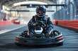 male racer in a helmet driving a go-kart on an indoor track looking at the camera
