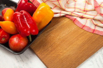 Cutting board with assort of different tomatoes and bell pepper on white wooden background..