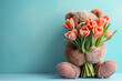 teddy bear with flowers. Teddy bear holding red tulips against natural blurred background, copy space. Cute bear with bouquet of red spring flowers. Post card or greeting card with plush teddy present