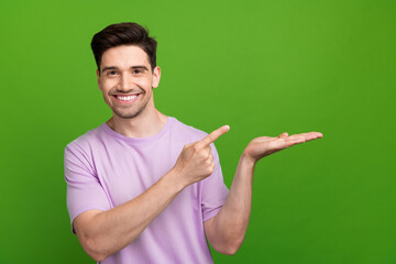 Canvas Print - Photo of cheerful man with brunet hair dressed purple t-shirt directing at offer on arm empty space isolated on green color background