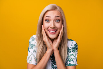 Wall Mural - Portrait of impressed nice girl with long hairstyle wear print blouse staring hands on cheekbones isolated on yellow color background