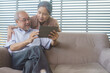 Asian grandfather and grandmother watching or meeting video call to family with digital tablet in the living room. Senior couple playing social media or searching on the internet.