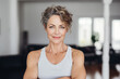 Beautiful smiling middle aged woman in white sport wear at home. Portrait of happy woman enjoying active lifestyle