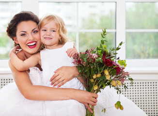 Smiling happy bride and a flower girl indoors