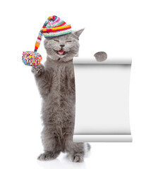 Poster - Happy cat wearing knitted warm woolen hat with pompon shows blank list. isolated on white background