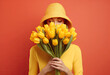 portrait of an elegant woman holding close to her face a bouquet of yellow tulips on red background