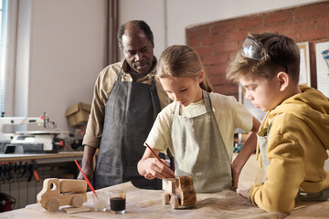 Wall Mural - Waist up portrait of young girl painting wooden toys in carpenting workshop for children, copy space