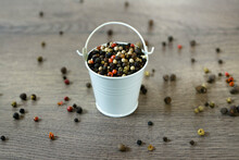 A Mixture Of Pepper Varieties With Peas In The Decorative Little White Bucket On The Wooden Background. Heap Of Various Pepper. Mix Of Red, Black, And White Peppercorn Seeds. Top View