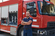 © .shock - Confident firefighter stands with crossed arms, exuding resilience and preparedness, ready to respond to emergencies alongside a modern fire truck, showcasing the heroism and strength of the fire