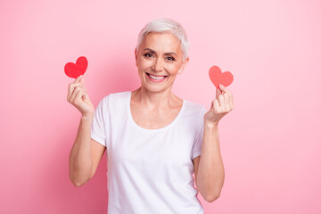 Poster - Photo portrait of pretty retired female hold two red heart postcards wear trendy white outfit isolated on pink color background