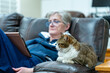 Lonely senior woman reading from a tablet with her cat- focus on the cat