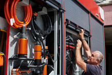A Dedicated Firefighter Preparing A Modern Firetruck For Deployment To Hazardous Fire-stricken Areas, Demonstrating Readiness And Commitment To Emergency Response