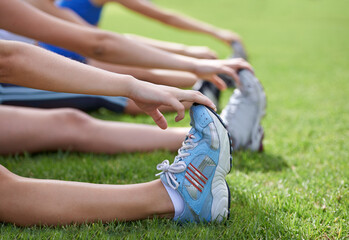 Stretching legs, sneakers and exercise in park, grass and nature with fitness group for health and wellness. People warm up for workout, training together with hands and shoes on grass outdoor