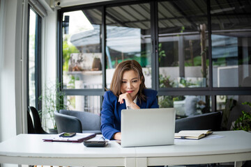 Wall Mural - Businesswoman sitting at desk on couch in workplace or at home working on laptop and analyzing data on charts and graphs and writing on papers to make business plan and strategies for company, 