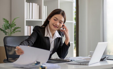 Wall Mural - Cheerful Asian businesswoman talking on the phone working in modern office Happy Asian businesswoman company manager wearing a suit is talking on the phone sitting in the office.