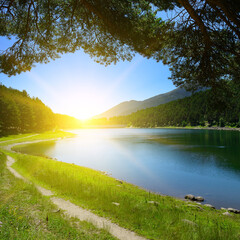 Wall Mural - Beautiful sunrise over blue lake and mountains covered with forest.