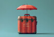 © Gayan - Vintage red suitcase with a red umbrella on top against a teal background, concept for travel and protection.