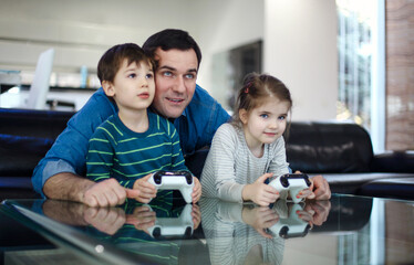 Smiling young man playing videogame together with son and daughter in modern living room