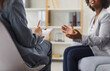Cropped portrait of a psychologist woman doctor making notes consulting female stressed patient during therapy session at office. Psychotherapy and mental health concept. Selective ficus.