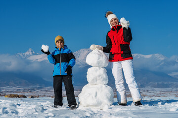 Wall Mural - Happy mom and son making snowman in the mountains