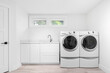 A laundry room with white cabinets and stainless steel faucet, white appliances, and brown tile flooring. No brands or names.
