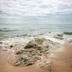 Black sea shore in sunny day. Stones covered with sand at the water`s edge. Summer seascape in bright delicate pastel colors.