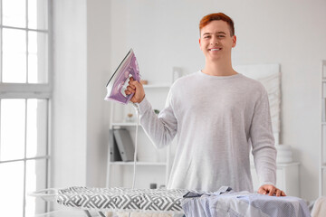 Wall Mural - Handsome young man with electric iron near ironing board in laundry room