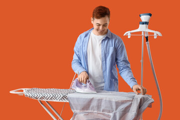 Wall Mural - Handsome young man ironing clothes on orange background