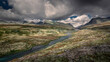 Rondane national park in Norway with winding lake and mountains on a cloudy sky