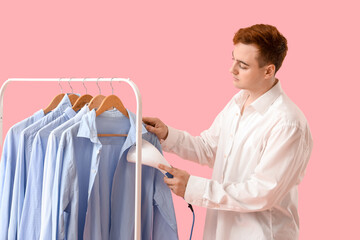 Wall Mural - Handsome young man steaming clothes with garment steamer on pink background