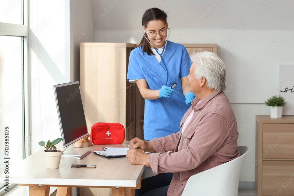 Senior man and nurse with stethoscope at home