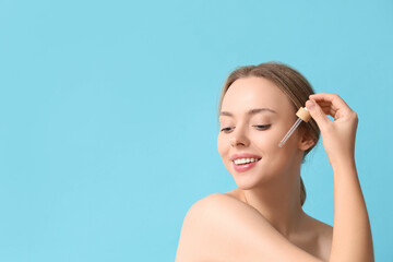 Poster - Beautiful young woman with cosmetic oil on blue background