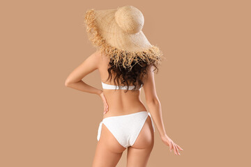 Wall Mural - Sexy young woman in swimsuit and straw hat on beige background, back view