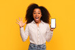 Excited black lady holding phone with blank screen on yellow background