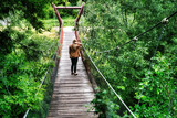 Fototapeta Mosty linowy / wiszący - Blond kobieta na wiszącym moście w lesie.
