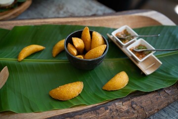 small yellow colombian empanadas served on top of banana leaf with various dipping sauces on the sides