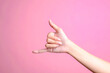 Woman hand showing calling hand gesture or shaka sign on pink background