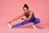 Fototapeta Panele - african american sportswoman stretching legs and hamstring muscles, pink background