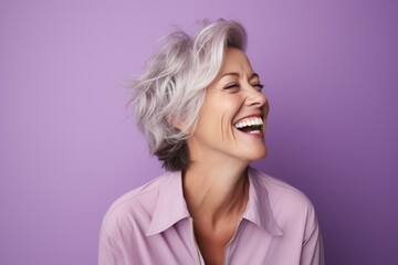 Wall Mural - Cheerful mature woman with short white hair laughing against purple background