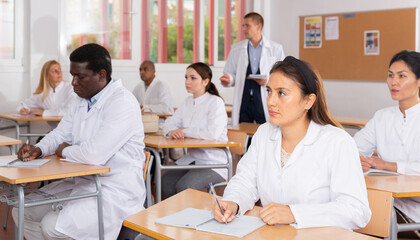 Wall Mural - International group of different age people in white coats sitting in lecture hall at refresher course