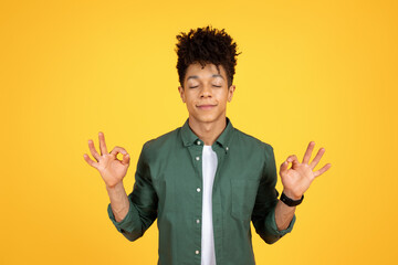 Wall Mural - Peaceful african american guy meditating on yellow background