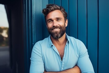 Wall Mural - Portrait of handsome young man with crossed arms standing against blue wall